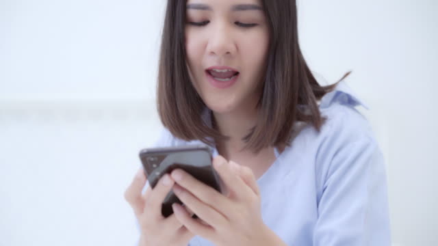 Junge-asiatische-Frau-mit-Smartphone,-während-auf-dem-Bett-nach-dem-Aufwachen-am-Morgen,-Schöne-attraktive-japanische-Mädchen-lächelnd-entspannen-im-Schlafzimmer-zu-Hause.-Spaß-im-Lifestyle-Frauen-zu-Hause-Konzept.