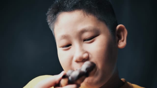 gran-construir-asiático-niño-preadolescente-comiendo-Donut-mientras-toca-su-barriga,-cámara-lenta-en-poca-luz.