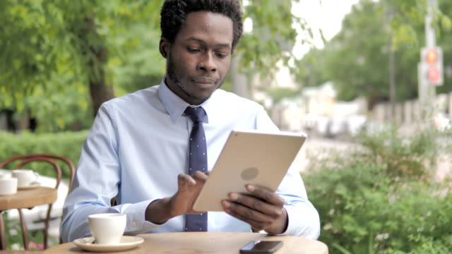 Hombre-de-negocios-africano-usando-la-tableta,-sentado-en-al-aire-libre-Cafe
