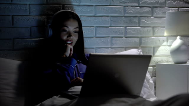 Smiling-woman-in-headphones-watching-video-at-night,-addiction-to-social-media
