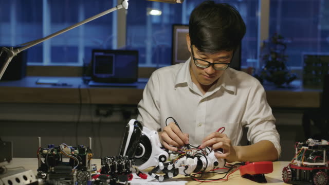 Jóvenes-ingenieros-de-desarrollo-de-electrónica-asiática-construyendo,-probando,-arreglando-robótica-en-el-laboratorio-de-investigación-en-ciencias-de-la-computación-por-la-noche.-Personas-con-concepto-de-tecnología-o-innovación.