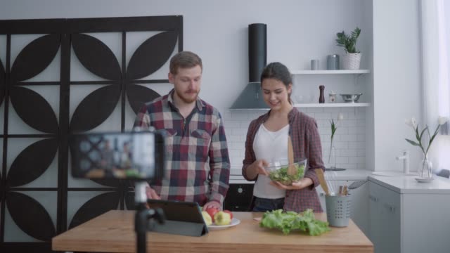 Ernährungsblog,-Vlogger-Mann-und-Frau-bereiten-gesundes-Frühstück-mit-Gemüse-und-Grüns-in-der-Küche,-während-Kamera-Smartphone-zeichnet-Video-für-Abonnenten-in-sozialen-Netzwerken