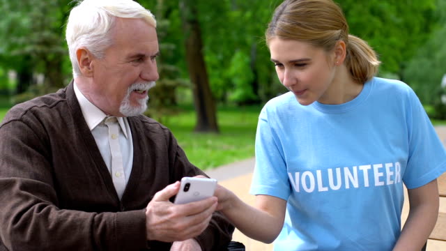 Freundliche-weibliche-Freiwillige-hilft-Rentnerin-im-Rollstuhl-verwenden-Smartphone-Charity-App