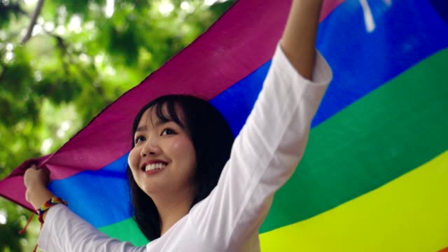 Retrato-de-joven-asiática-ondeando-bandera-lgbt-arco-iris-en-el-parque,-cámara-lenta