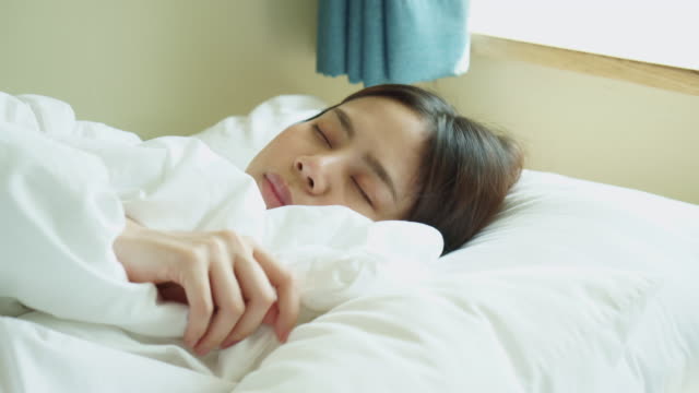 Young-Asian-woman-waking-up-in-the-morning-and-using-smartphone-on-the-bed-room.
