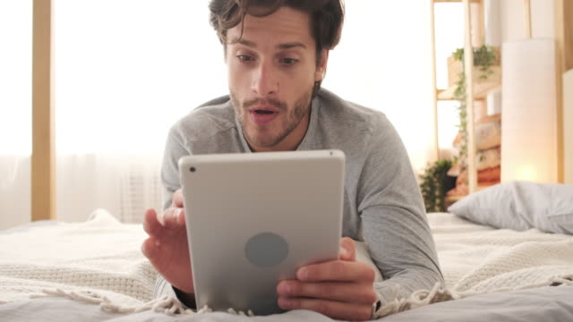 Hombre-feliz-usando-tableta-digital-en-la-cama