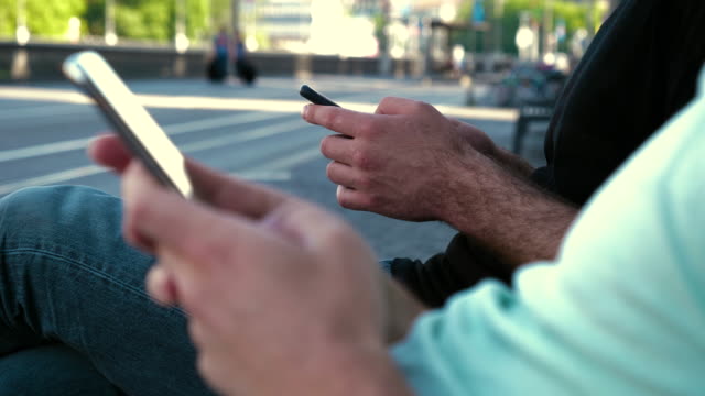 Männer-mit-Smartphone-auf-einer-Bank-sitzend