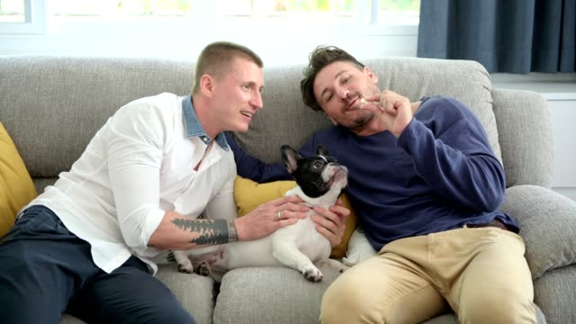 Gay-couple-relaxing-on-couch-with-dog.-Feeding-dog.