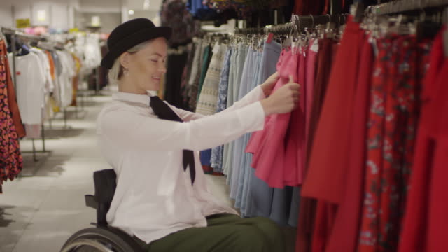 Glückliche-Frau-im-Rollstuhl-Einkaufen-für-Röcke-im-Bekleidungsgeschäft