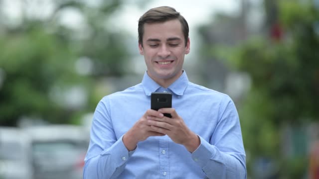 Happy-young-handsome-businessman-using-phone-outdoors
