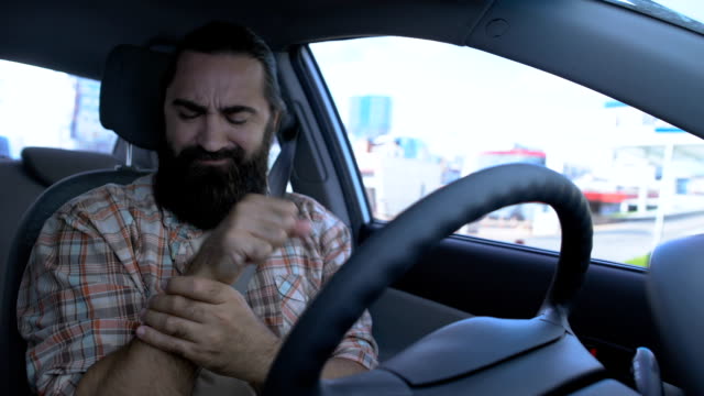 Hombre-barbudo-masajeando-la-muñeca-mientras-conduce-el-coche,-la-mano-lesionada,-inflamación-de-las-articulaciones