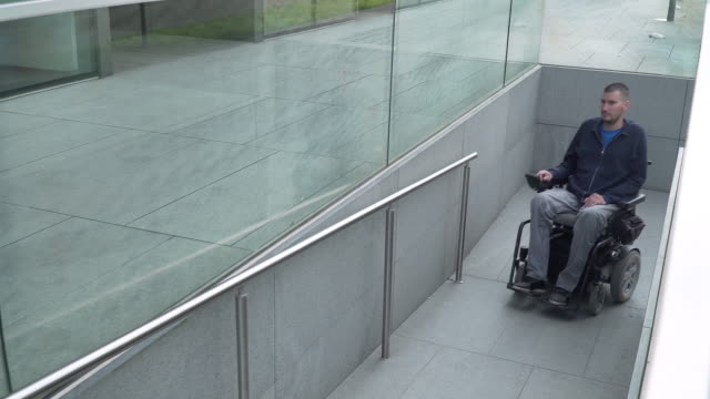 4k-Auflösung-folgen-von-einem-Mann-auf-elektrischen-Rollstuhl-über-eine-Rampe.-Barrierefreiheitskonzept