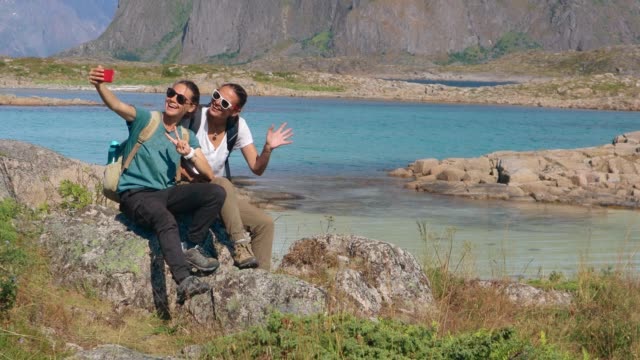 Dos-jóvenes-blogueras-tomando-un-selfie-con-vistas-a-un-fiordo-noruego-con-un-teléfono-inteligente.