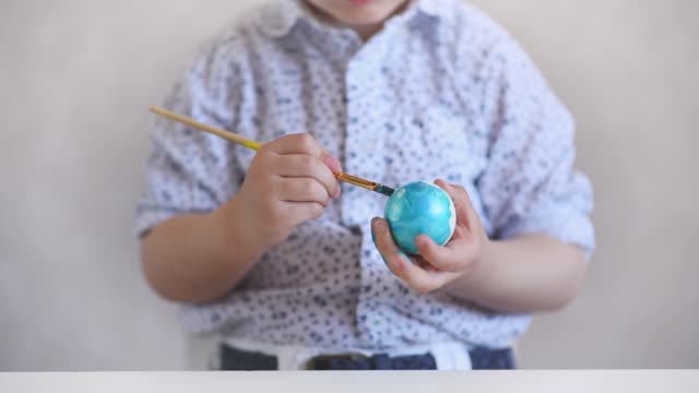 A-little-child-paints-an-one-easter-egg-at-the-table-on-a-white-background.