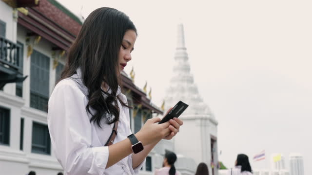 Junge-asiatische-Frau-mit-einem-Smartphone,-während-auf-der-Straße-neben-Wat-Phra-Kaew-in-Thailand-stehen-und-Spaß-in-der-Urlaubszeit.