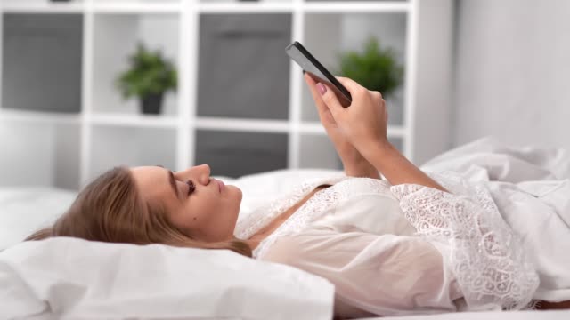 Entspannte-Frau-liegt-auf-bequemen-Bett-chatten-mit-dem-Smartphone.-Mittlere-Nahaufnahme-auf-4k-RED-Kamera