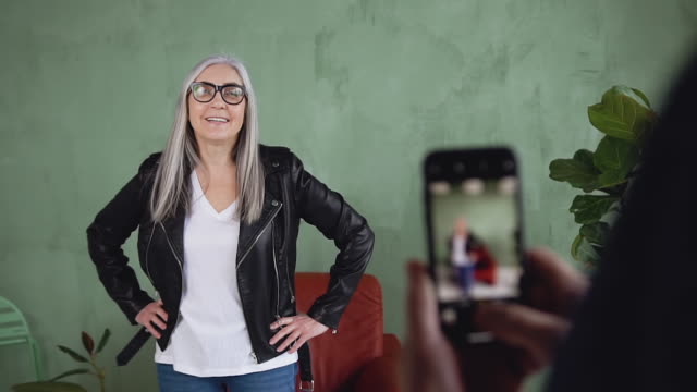 Lächelnd-entzückende-moderne-trendige-Frau-in-Brille,-die-Foto-auf-dem-Handy-von-jemandem-auf-der-grünen-Wand-Hintergrund