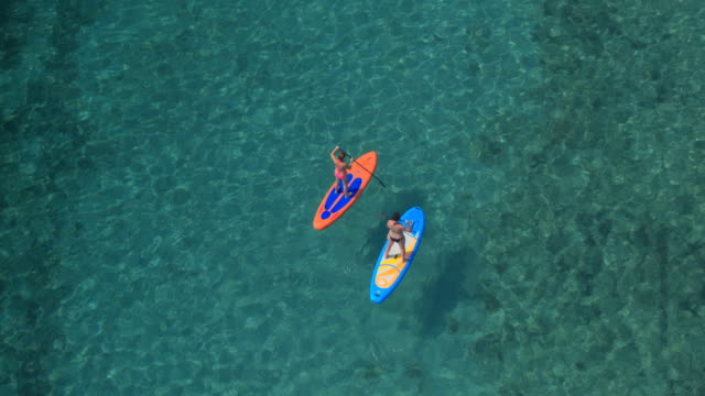 Antenne:-Zwei-Freundinnen-aufstehen-Paddle-boarding-in-atemberaubenden-kristallklares-Meer