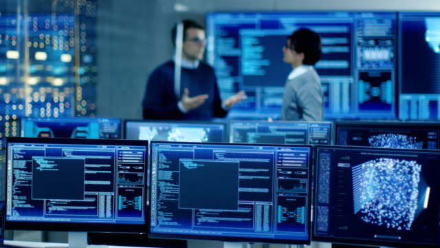 In-the-Data-Center-System-Control-Room-Monitors-Show-Work-Done-on-Neural-Networking,-AI-integration-and-Data-Mining.-In-the-Background-Two-Specialists-Talking.