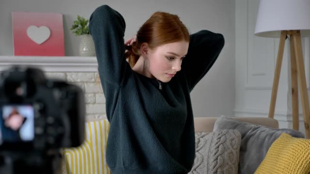 Young-red-haired-girl-blogger,-smiling,-talking-at-the-camera,-Makes-herself-a-hairstyle,-tress,-home-comfort-in-the-background.-60-fps