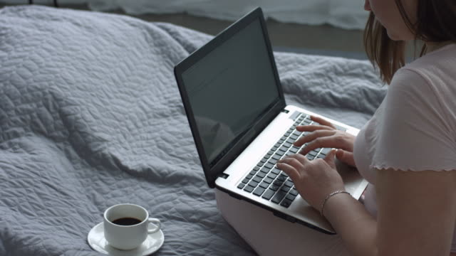 Positive-Frau-mit-Laptop-Blogging-auf-dem-Bett