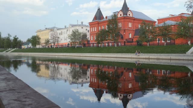 City-Quay-in-the-spring.-Symmetry-in-the-reflection-of-buildings-and-people-in-the-river.-The-building-is-in-the-form-of-a-castle-from-a-red-brick