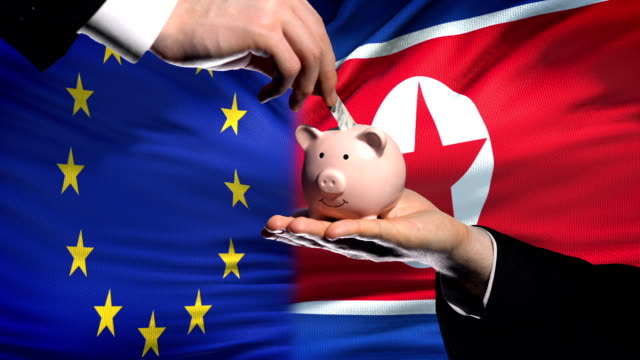 EU-investment-in-North-Korea,-hand-putting-money-in-piggybank-on-flag-background