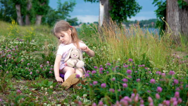 Una-niña-jugando-con-un-conejo-de-juguete-en-el-Prado-entre-el-trébol-de-flores
