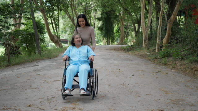 Ältere-Frau-mit-ihrer-Tochter-schieben-Rollstuhl-durch-den-park
