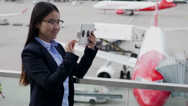 Señora-asiático-feliz-comunicarse-por-mensajería-en-tableta-en-aeropuerto