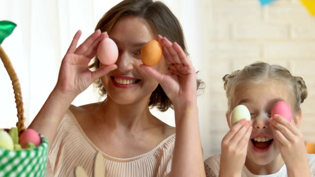 Niedliche-Tochter-und-Mutter-setzen-bunte-Eier-in-die-Augen,-Osternacht-Spaß
