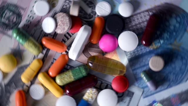VIDEO,-cuidado-de-la-salud-costo-concepto-con-diversas-pastillas-y-fármacos-girando-sobre-dinero-en-efectivo