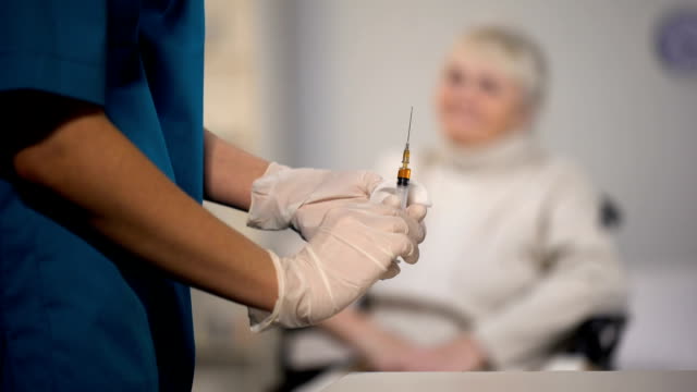 Nurse-making-injection-to-elderly-woman,-treatment-in-hospital,-health-care