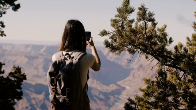 Vista-de-vuelta-feliz-mujer-turista-senderismo,-tomando-foto-del-teléfono-inteligente-del-increíble-paisaje-de-montaña-del-Parque-Nacional-del-gran-cañón.