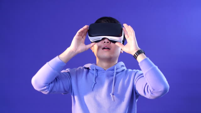 Fröhliche-japanische-Jugendliche,-die-Videospiel-in-virtueller-Reality-Helm-auf-dunkelblauem-Hintergrund-spielen