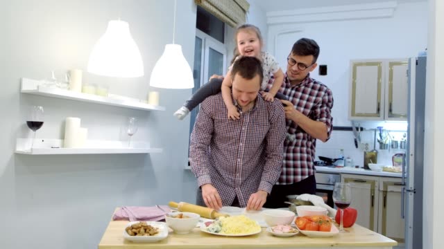 Familia-gay-con-hija-niño-cocinar-pizza-juntos-en-la-cocina-y-abrazando.