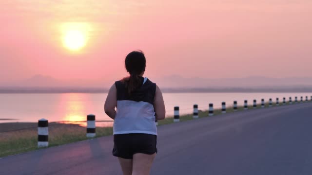 Mujeres-asiáticas-con-sobrepeso-corriendo-en-la-calle-en-la-luz-del-sol-temprano-por-la-mañana.-concepto-de-perder-peso-con-ejercicio-para-la-salud.-Cámara-lenta,-vista-posterior
