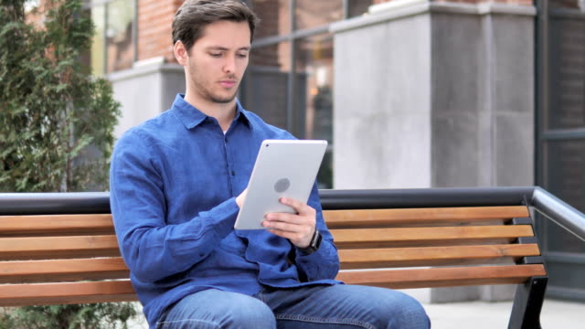 Junger-Mann-nutzt-Tablet-beim-Sitzen-auf-Bank