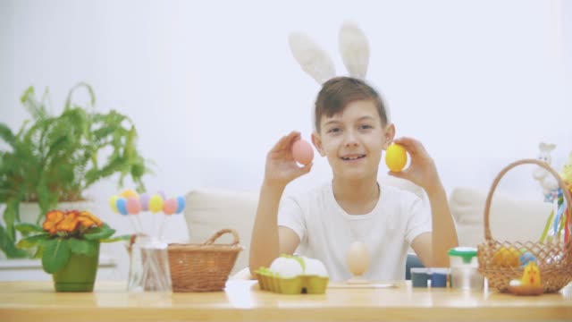Little-cute-and-adorable-boy-is-smiling-and-playing-with-colorful-chicken's-eggs-in-his-hands.-Concept-Easter-holiday.