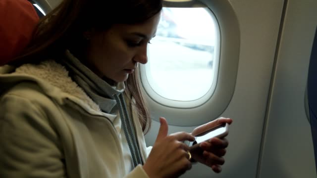Retrato-chica-joven-viaja-en-avión,-se-sienta-cerca-de-la-ventana-y-utiliza-el-teléfono