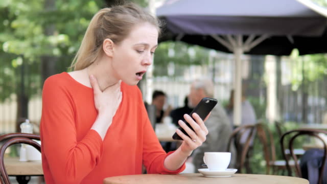Young-Woman-Upset-by-Loss-on-Smartphone,-Sitting-in-Cafe-Terrace