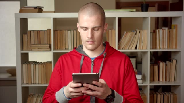 Closeup-portrait-of-young-attractive-caucasian-male-student-using-the-tablet-in-the-college-library-indoors