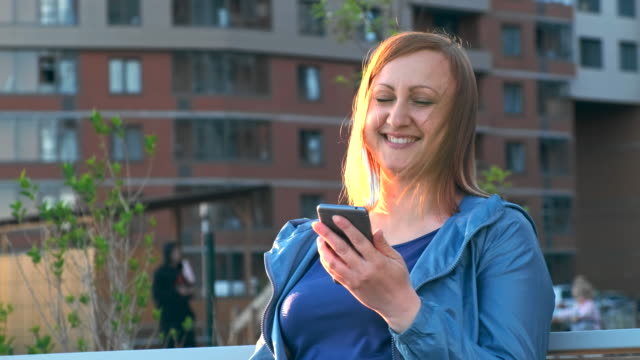 Frau-mit-Smartphone-auf-Bank-in-der-Stadt-sitzen