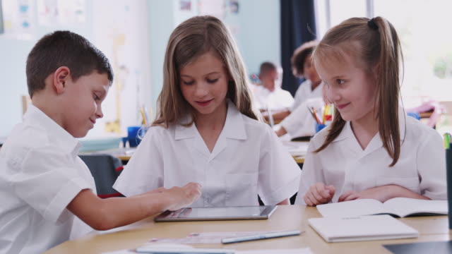Drei-Grundschüler-tragen-Uniform-mit-digitalem-Tablet-am-Schreibtisch