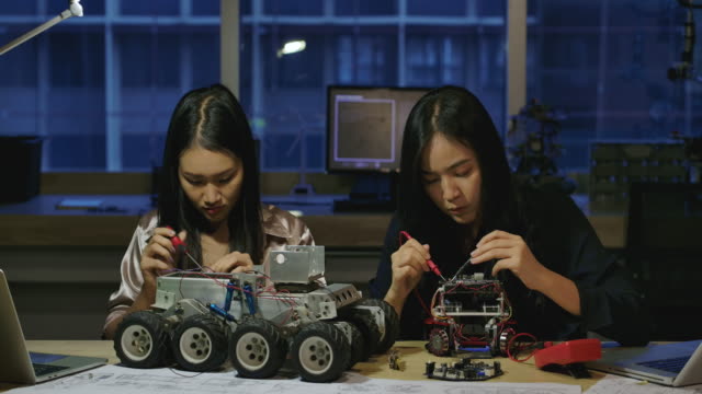 Team-of-young-electronics-development-engineers-building,-testing,-fixing-robotics-prototype-at-night-in-laboratory.-People-with-technology-or-innovation-concept.