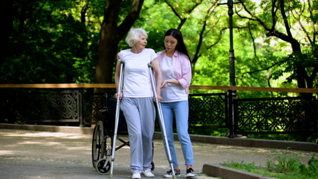 Mujer-joven-ayudando-a-la-anciana-caminando-con-muletas,-rehabilitación-de-fractura-de-cadera