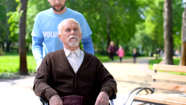 Männliche-Freiwillige-kümmern-sich-um-ältere-behinderte-Patienten,-verbringen-Zeit-im-Park