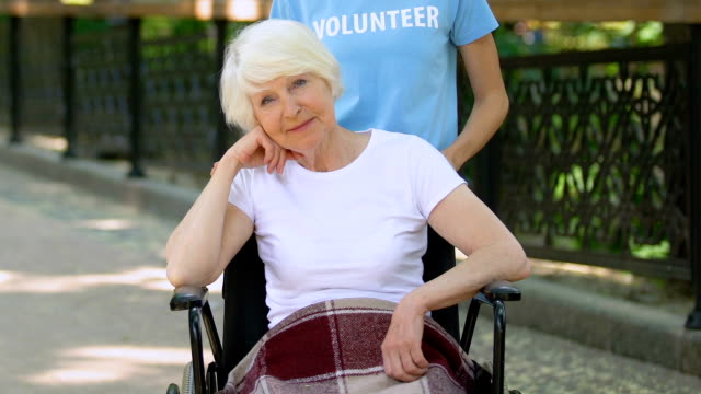 Volunteer-supporting-handicapped-old-patient-in-wheelchair,-day-in-hospital-park