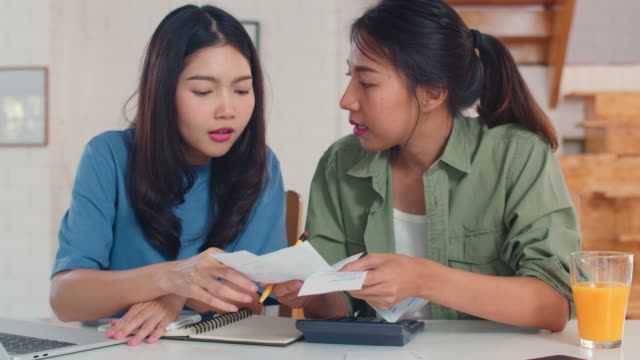 Business-Asian-Lesbian-couple-using-calculator-record-budget,-tax,-financial-document-on-laptop-working-in-kitchen.