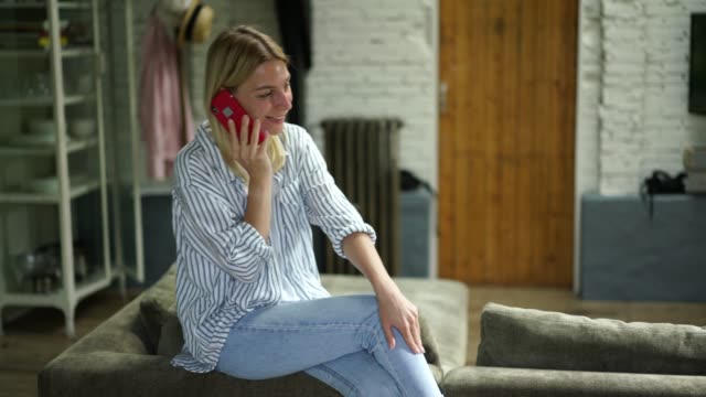 25-Jahre-alt-lächelnde-kaukasische-Frau-in-Lässigkeit-tragen-Handy-Gespräch,-während-auf-dem-Sofa-sitzen
